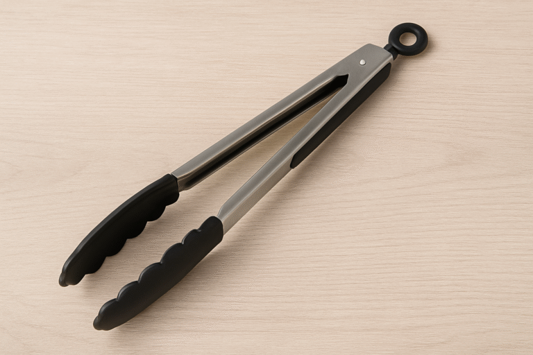 A pair of stainless steel tongs with black silicone tips and handle rests on a light wood surface, perfect for use as kitchen tongs or serving tongs.